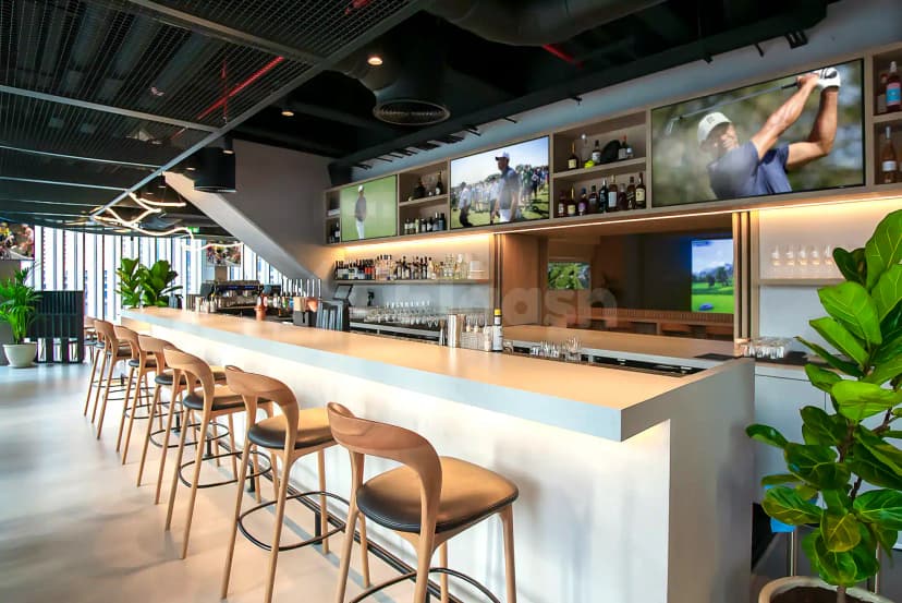 Bar counter at Bedrock Pier 7 in Dubai featuring mounted TV screens showing golf footage and backlit shelves