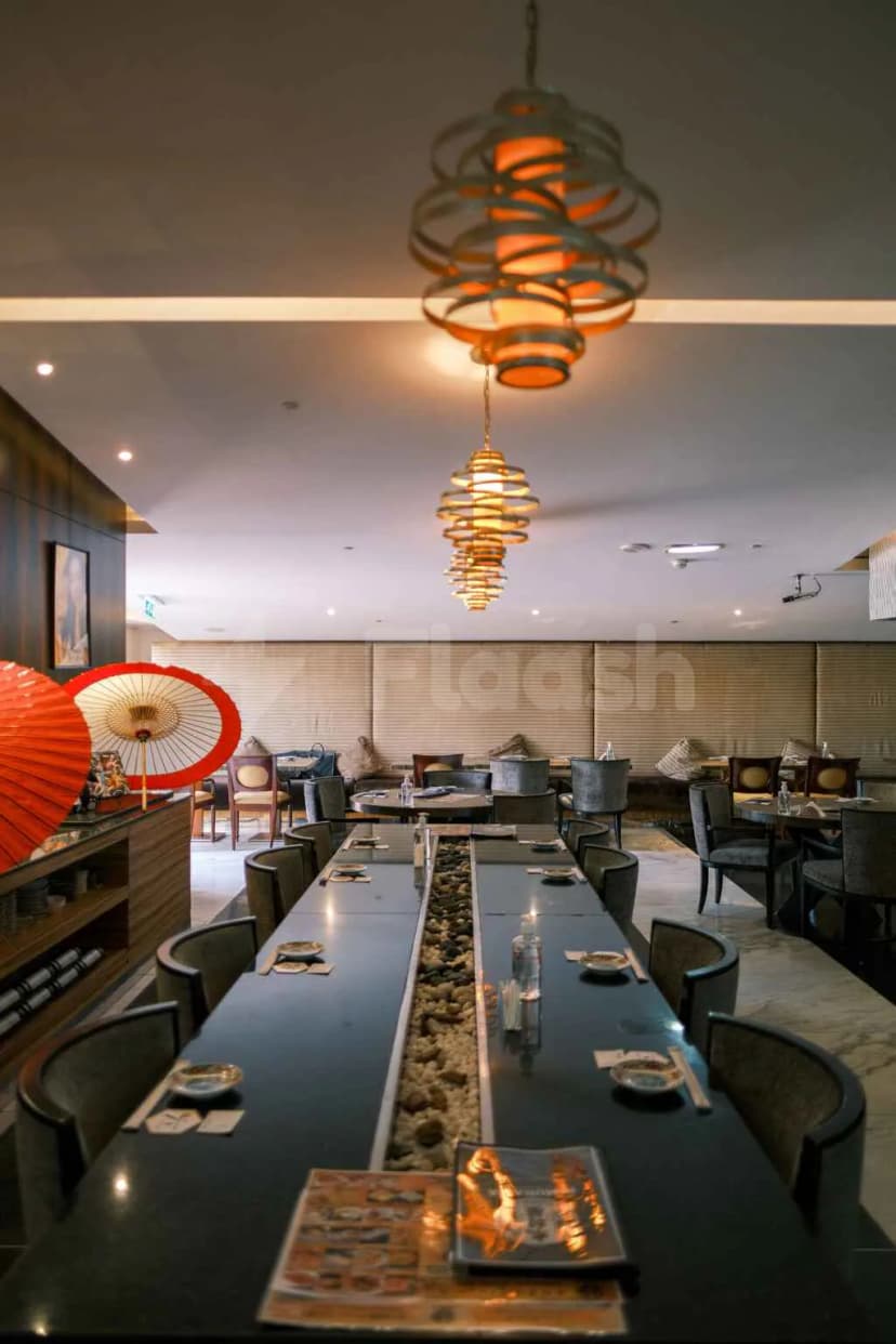 Long black dining table with stone-filled runner at Kimuraya Authentic Japanese Restaurant Downtown Dubai, featuring spiral pendant lights