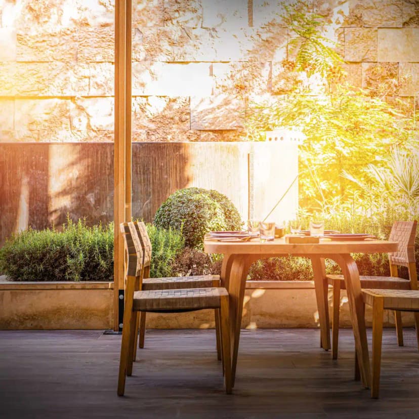 Terrace at Suhail Arabic Restaurant Riyadh featuring a wooden dining table, woven leather chairs, stone wall, and green