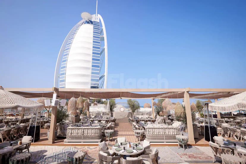 Rooftop terrace at Verde Beach Restaurant Dubai featuring a wooden deck, woven umbrellas, and the Burj Al Arab