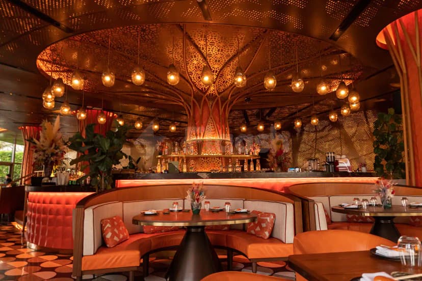 Restaurant interior at Sushisamba Lusail featuring a central ornate laser-cut metal canopy and curved booth seating with orange