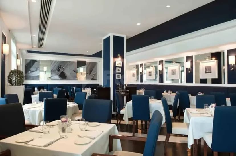 Restaurant interior at Bice Mare Restaurant Dubai featuring white tablecloths, blue upholstered chairs, framed artwork, and wall mirrors