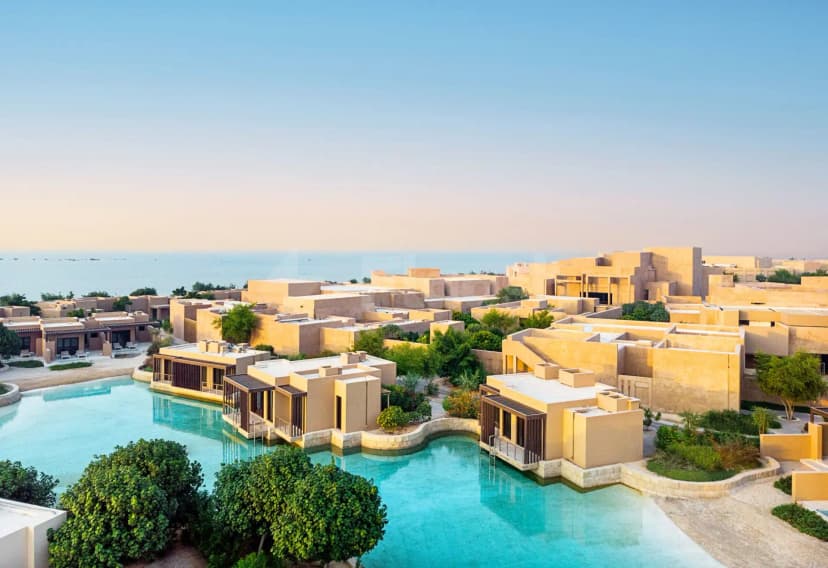 Turquoise swimming pool surrounded by beige stone buildings with wooden slatted screens at Zulal Wellness Resort in Doha