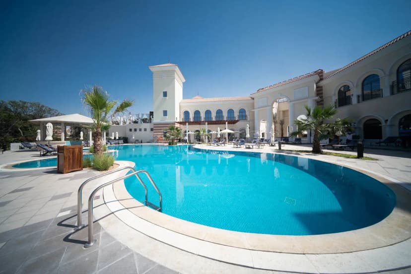 Large swimming pool at The Els Club Dubai Sports City with curved edge and palm trees
