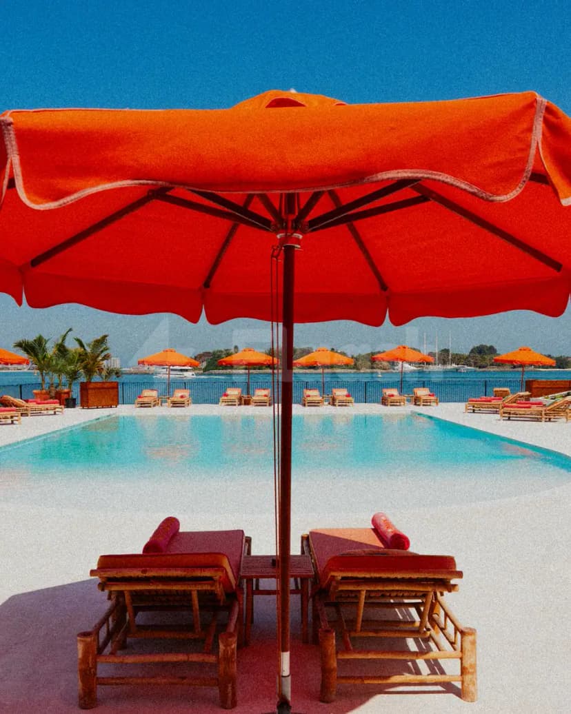 Swimming pool at Tagomago Dubai featuring a rectangular blue pool, white deck, and orange sun umbrellas with wooden