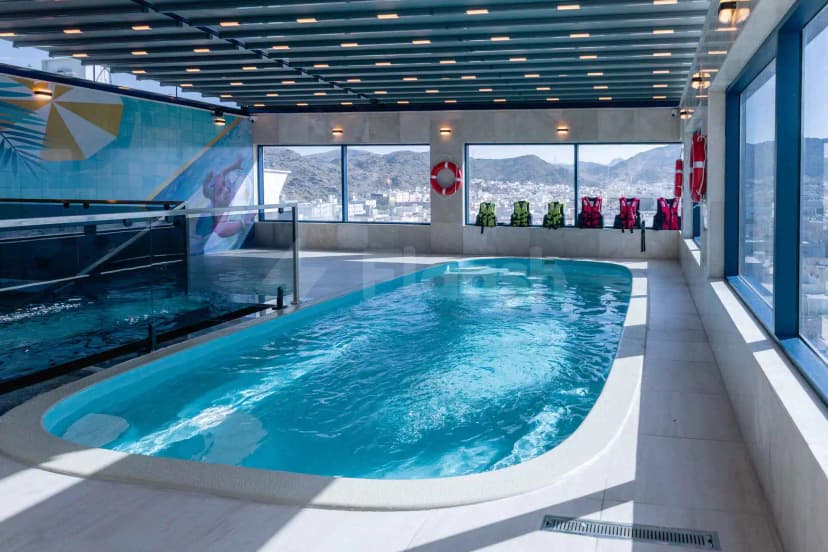 Indoor swimming pool at Swiss International Taif in Taif with turquoise water, large windows offering mountain and city