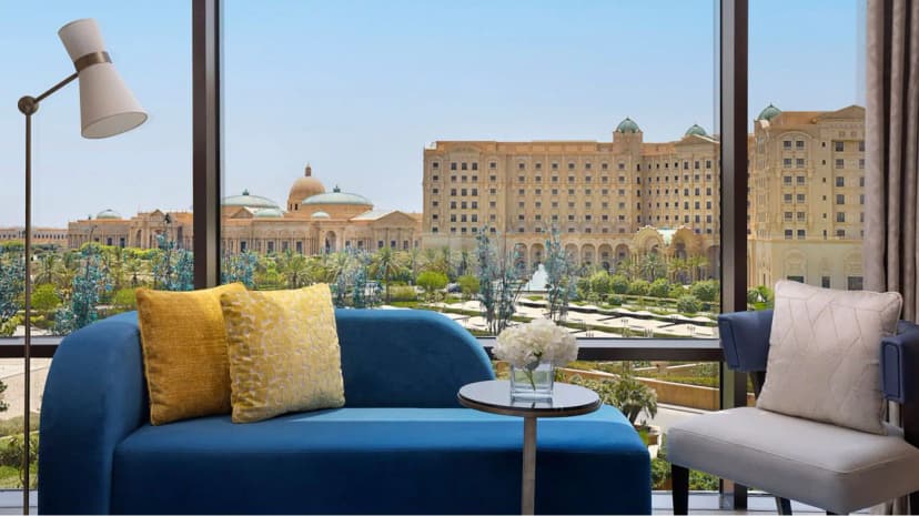Meeting room at The St. Regis Riyadh featuring a blue velvet sofa and large windows overlooking the palace