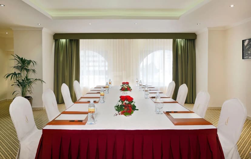 Meeting room at City Seasons Al Hamra Hotel Abu Dhabi with long table, white chairs featuring gold embroidery