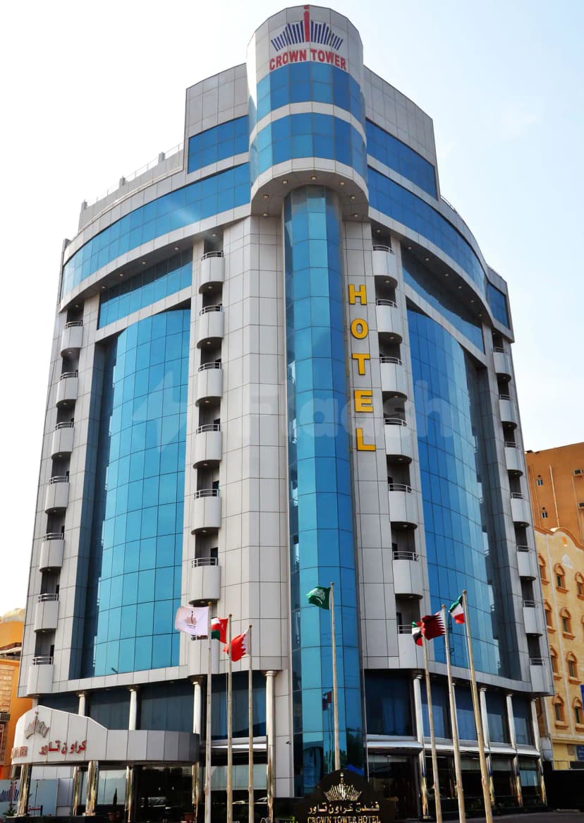 Hotel facade of Crown Tower Al Jubail featuring blue glass panels, white stone cladding, and a vertical yellow