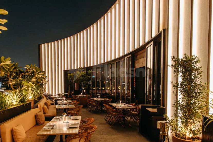 Rooftop terrace at Chez Wam in Dubai featuring a curved illuminated wall and potted plants alongside set dining