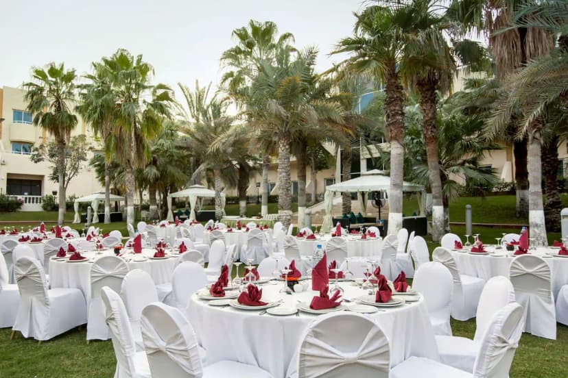 Outdoor dining area at Metropolitan Al Mafraq Hotel in Abu Dhabi with round tables, white chair covers, red