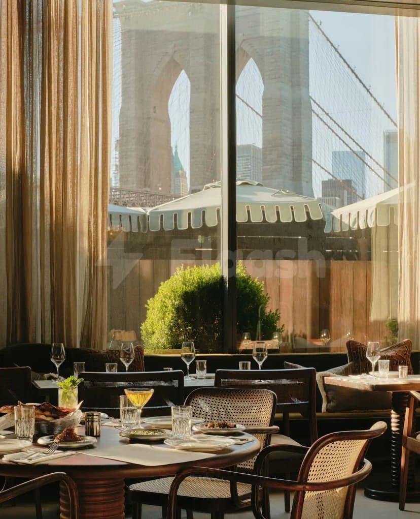 Restaurant interior at Berenjak Acurio Restaurant Dubai with large windows framing the Brooklyn Bridge view and cane-back chairs