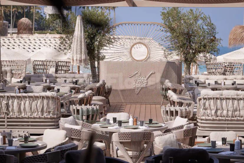 Outdoor dining area at Verde Beach Restaurant Dubai featuring a woven wall panel with sunburst mirror and olive