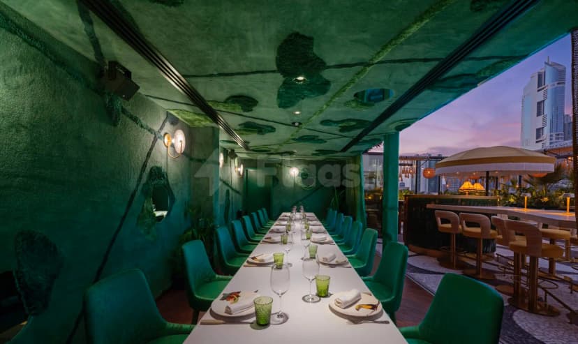 Long white dining table in Amazónico Dubai with green textured walls and ceiling, city skyline visible