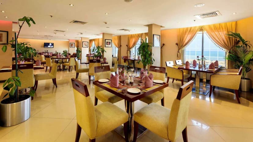 Restaurant at Coral Jubail in Al Jubail featuring set dining tables with pink napkins and large windows offering