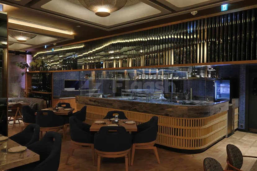 Open kitchen with glass partition and wooden counter at Robata Riyadh, featuring a mirrored slatted wall and herringbone