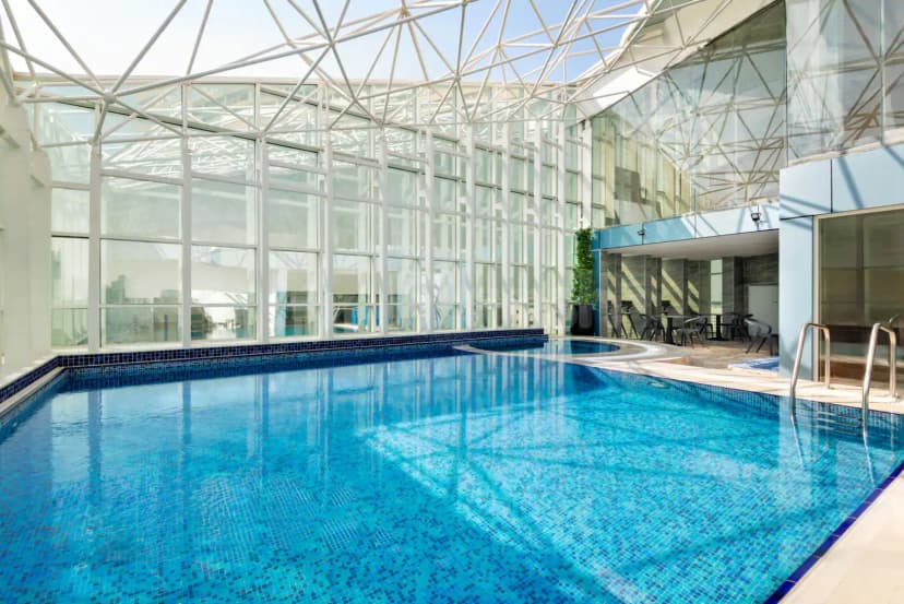 Indoor swimming pool at La Quinta by Wyndham Abu Dhabi Al Wahda featuring a white geometric glass roof