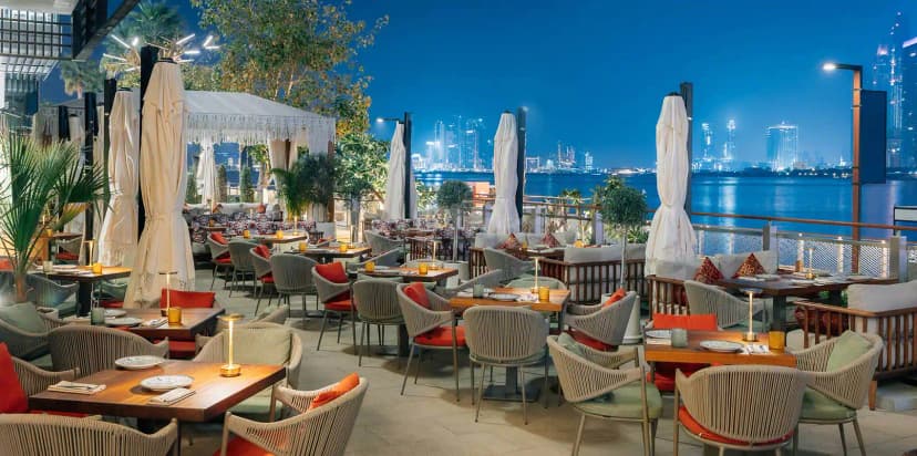 Rooftop terrace at Grand Zor Restaurant Dubai with wooden tables, wicker chairs, and a city skyline view