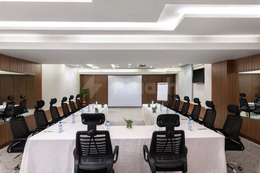 Boardroom at Warwick Hotel Jeddah with u-shaped table layout, white patterned tablecloth, black mesh chairs, wooden wall paneling