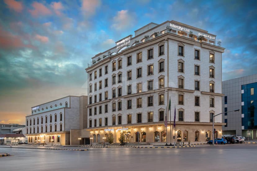 Hotel facade of Intercity Hotel Riyadh featuring white stone cladding, arched windows with black grilles, and illuminated bilingual
