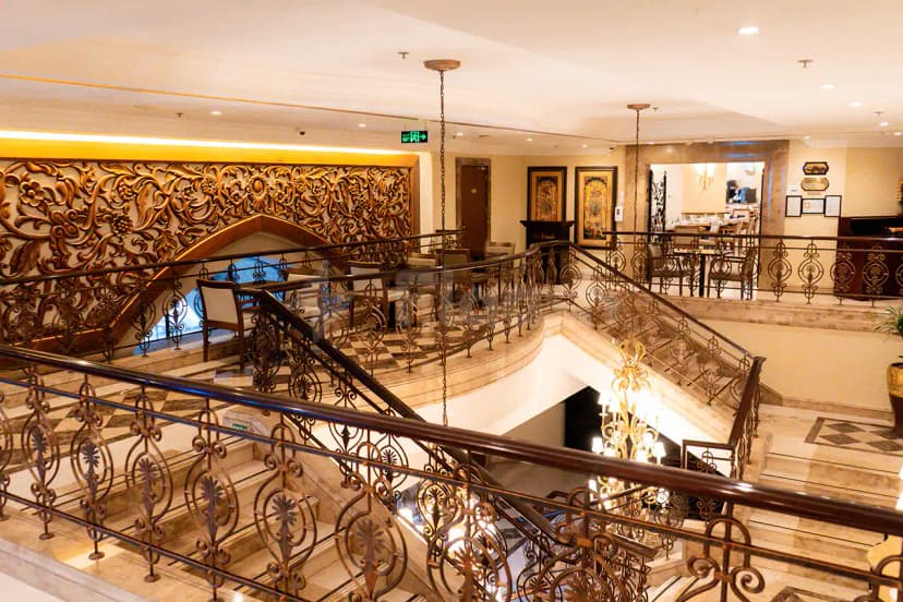 Entrance hall at Sheraton Khalidiya Abu Dhabi featuring an ornate wooden wall panel and a curved marble staircase