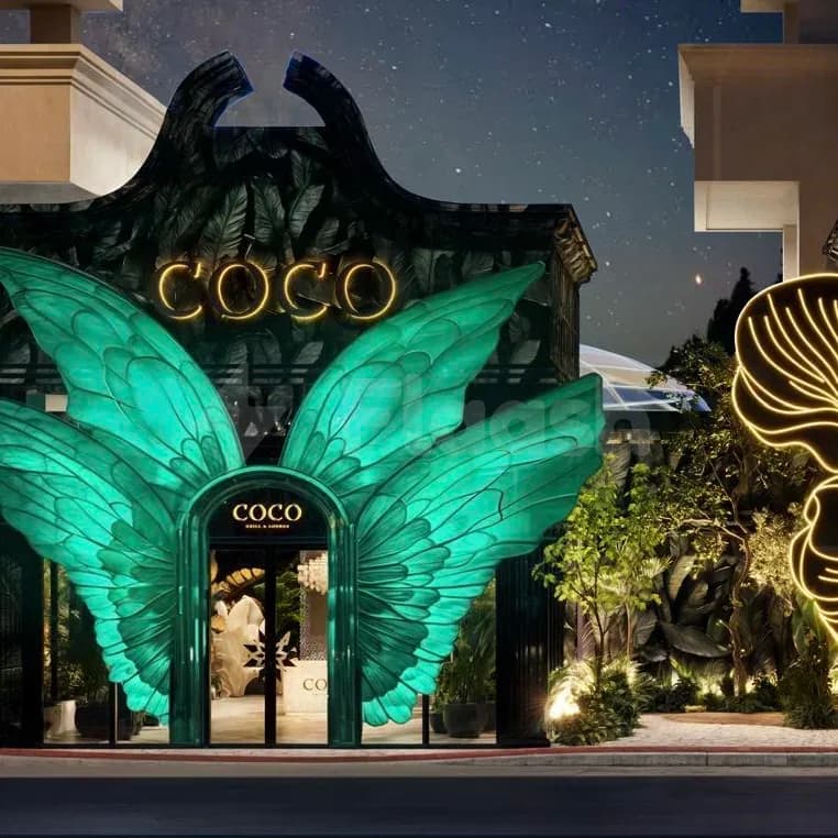 Illuminated facade at Coco Restaurant Al Murooj in Dubai with large green wing sculpture