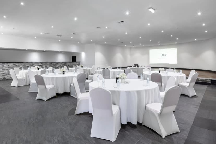Ballroom at BM Beach Resort Ras Al Khaimah with round tables, white chair covers, and a projector screen