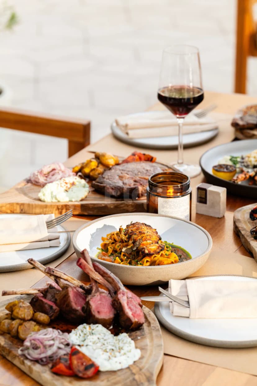 Restaurant table at Ergon Deli & Cafe Abu Dhabi with grilled lamb chops, pasta, and red wine in natural