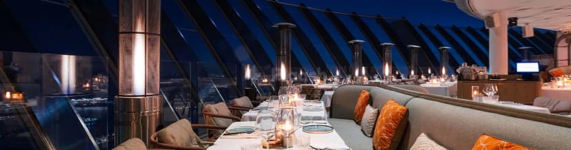 Rooftop terrace at Coucou Dubai featuring glass railings, metal patio heaters, and a city night view under