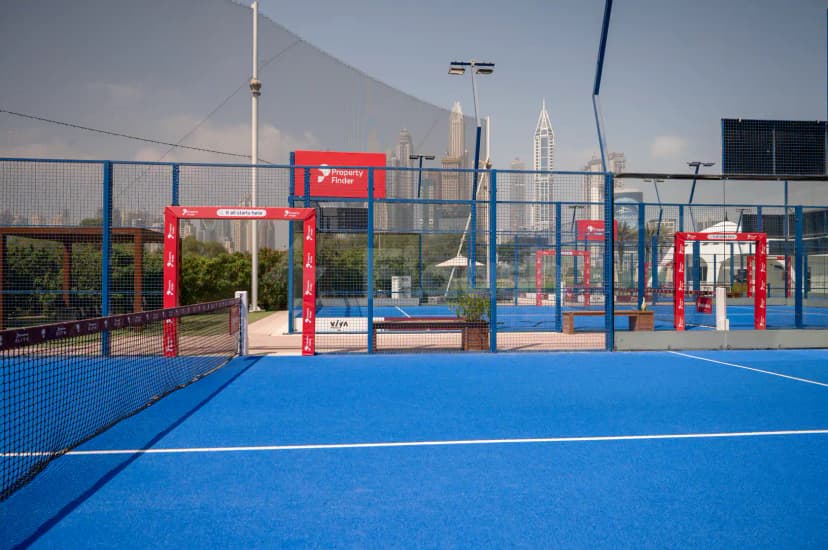 Blue padel court at Emirates Golf Club in Dubai with red Property Finder archway and city skyline visible