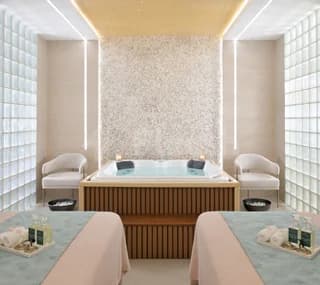 Indoor spa room at Swissotel Al Murooj Dubai featuring a rectangular hot tub with wooden paneling and white