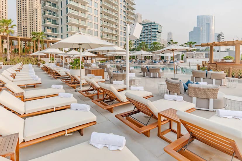 Rooftop terrace at Cove Beach Dubai featuring wooden sun loungers with cream cushions and white umbrellas overlooking