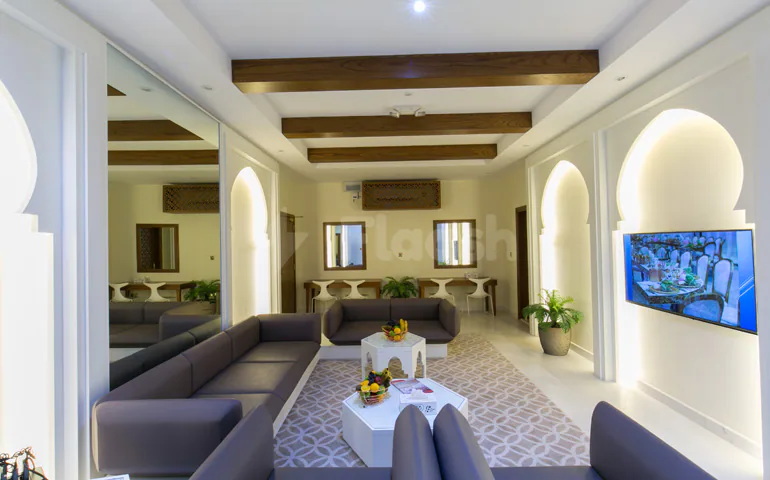 Meeting room at Al Jewan Hall Doha featuring arched doorways, wooden ceiling beams, and grey leather sofas arranged