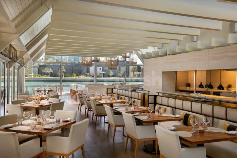Brauhaus Restaurant Abu Dhabi features a modern dining space with wooden tables, beige upholstered chairs, and large windows
