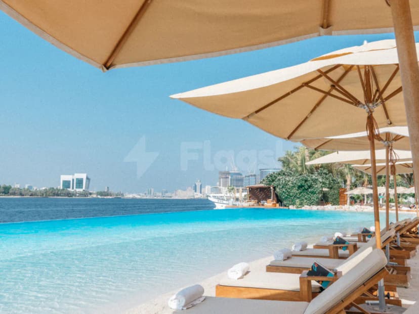Infinity pool at Twiggy Dubai with turquoise water extending to the city skyline, lined with wooden lounge chairs