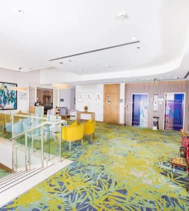 Entrance hall at Mena Plaza Hotel Albarsha in Dubai featuring a glass railing and yellow armchairs near