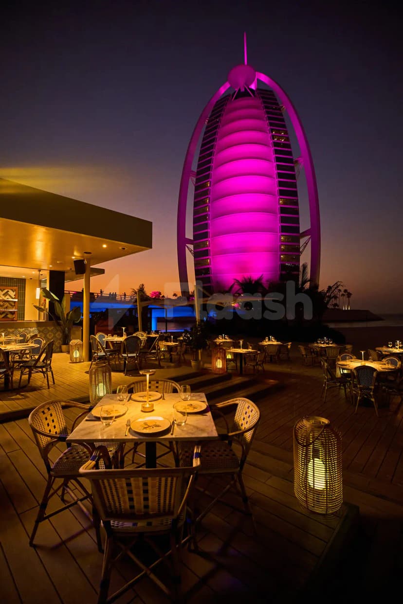 Rooftop terrace at Lucia's Mare Restaurant Dubai featuring wooden decking, wicker chairs, and a purple-lit sail-shaped building facade