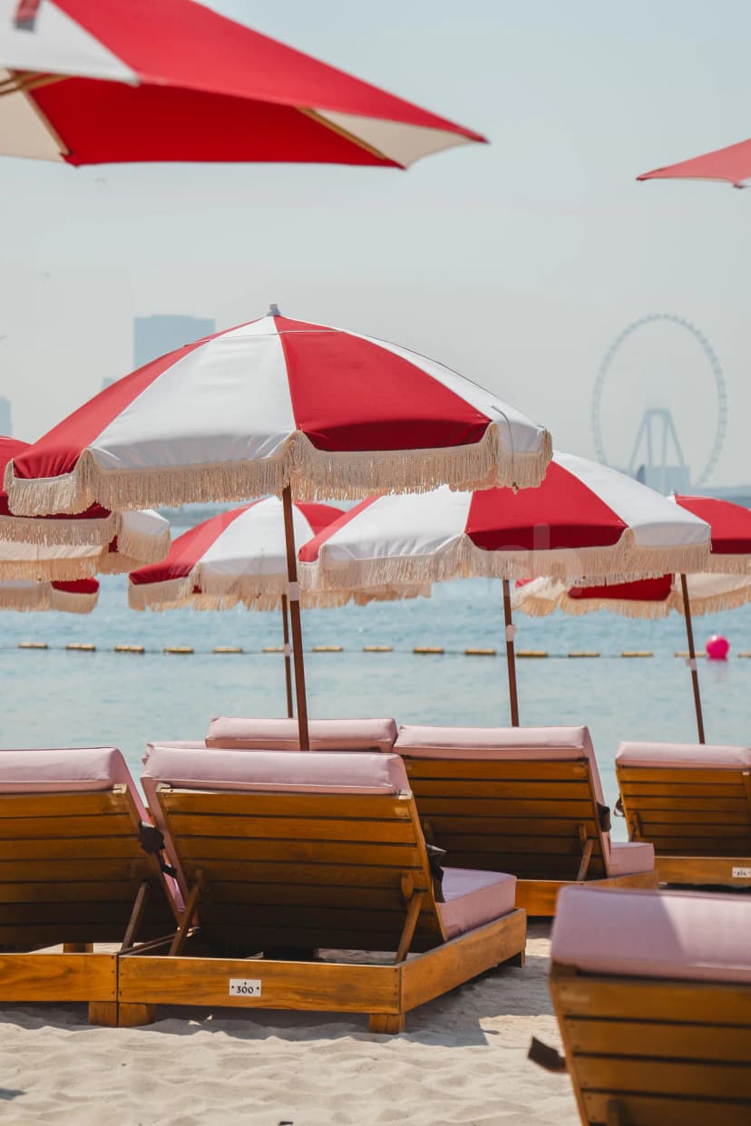 Beach at February 30 in Dubai with wooden lounge chairs, pink cushions, and red-and-white fringed umbrellas overlooking