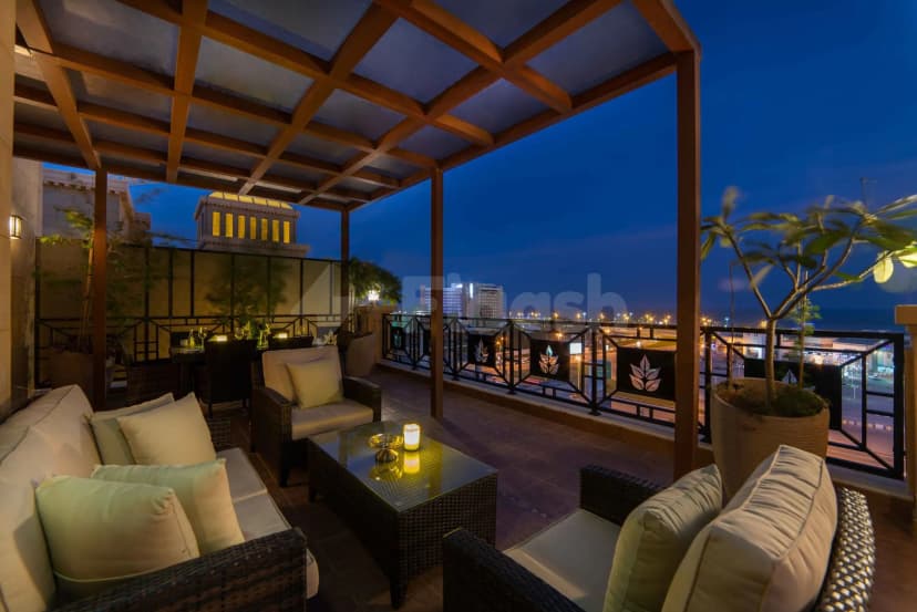 Rooftop terrace at Warwick Al Khobar featuring a wooden pergola, black metal railing with leaf motifs, and city