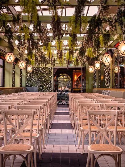 Ballroom at Swingers The Crazy Golf Club Dubai with rows of wooden chairs, hanging green plants