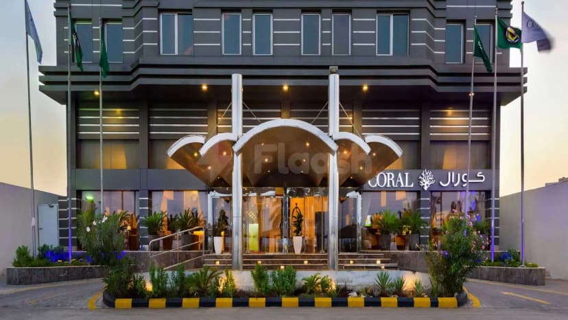Hotel facade of Coral Jubail in Al Jubail featuring a glass entrance with arched metal canopy and illuminated